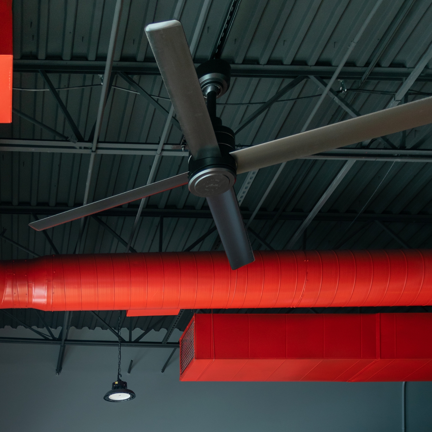 Ventilateur Hunter TRAK Edge et gaine de ventilation rouge sous un plafond de local tertiaire
