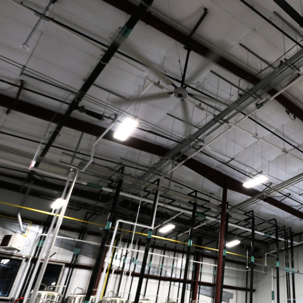 Déstratificateur HVLS noir sous la charpente métallique d'un grand volume éclairé