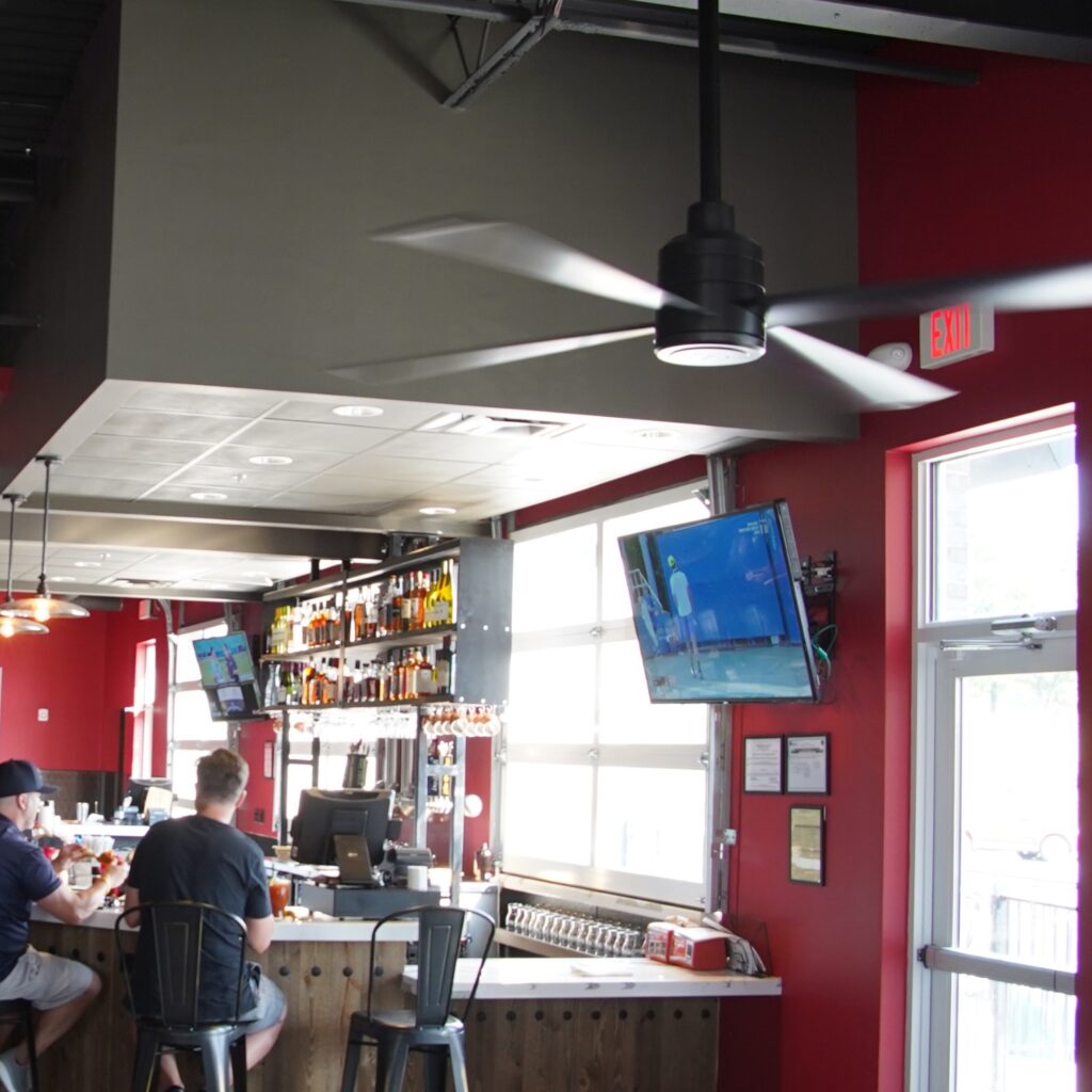 Ventilateurs Hunter TRAK Edge noirs dans la salle d'un bar-restaurant équipé d'écrans