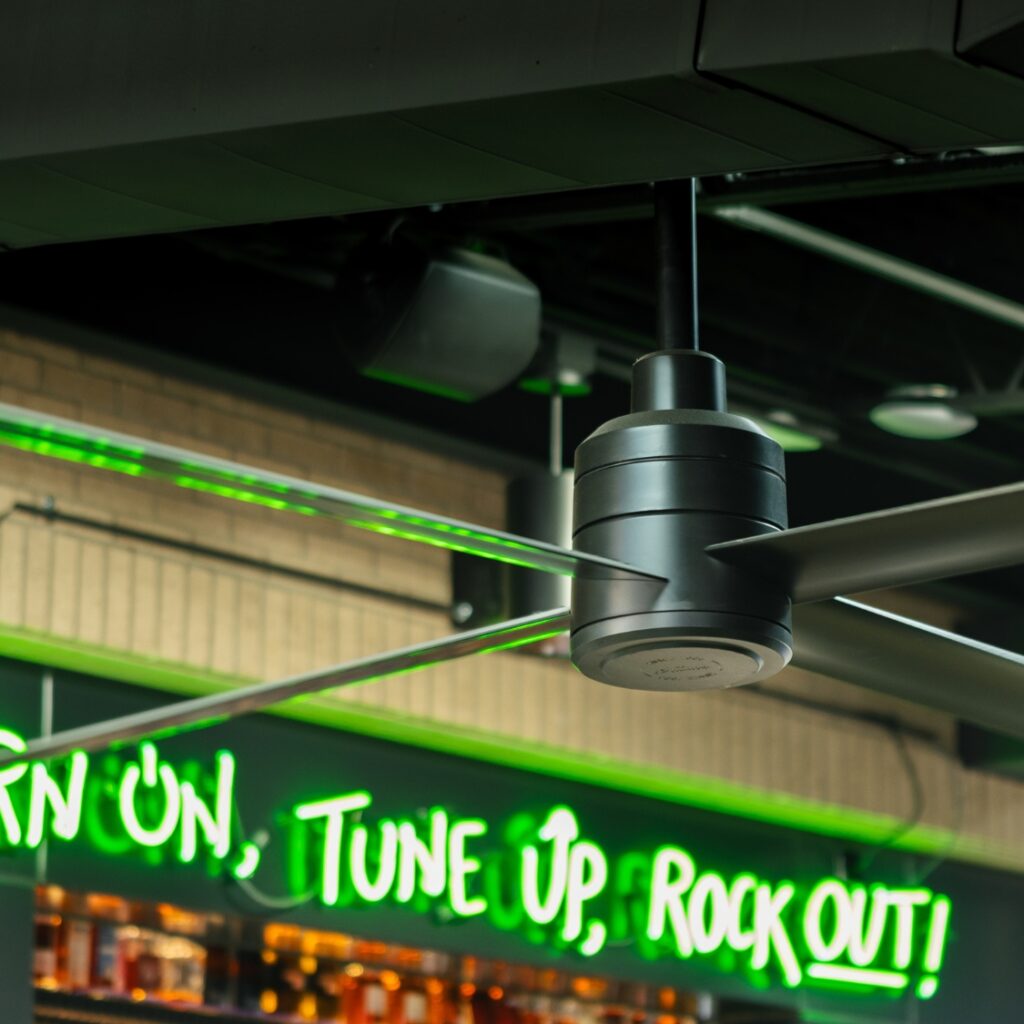 Ventilateur Hunter TRAK Edge noir dans un bar-lounge, bouteilles alignées en arrière-plan