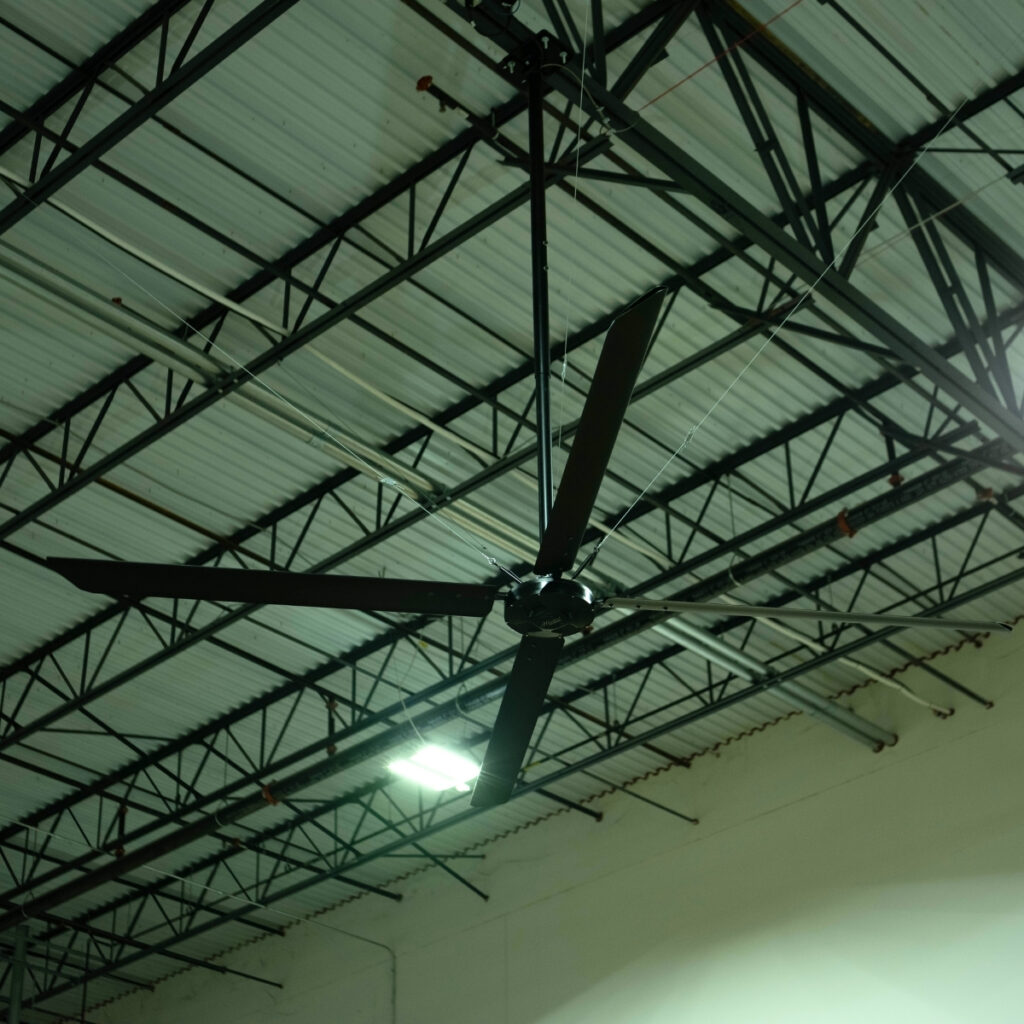 Déstratificateur HVLS noir sous la charpente métallique sombre d'une salle multisport