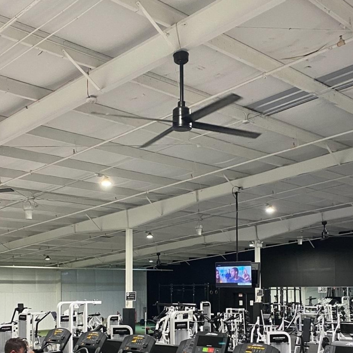 Ventilateur Hunter TRAK Edge brassant l'air d'une salle de sport équipée d'appareils de fitness